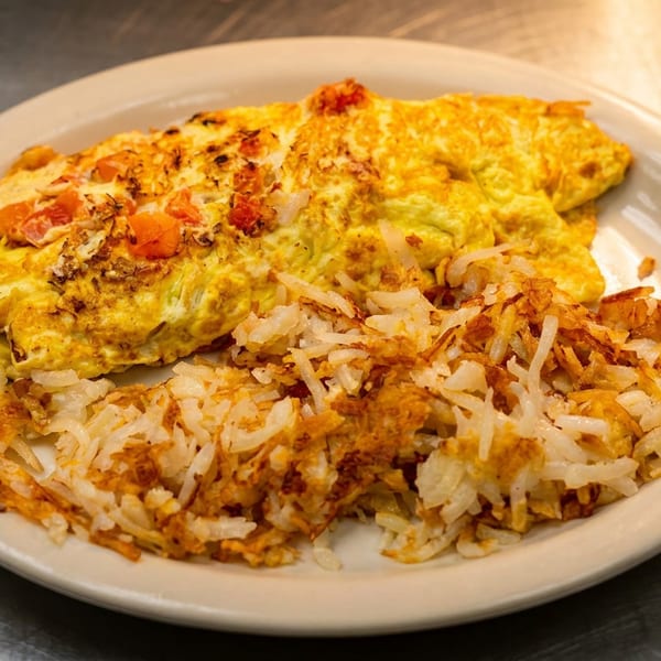 Plate of fluffy omelets topped with tomatoes and herbs, served alongside crispy golden rice in a casual restaurant setting.