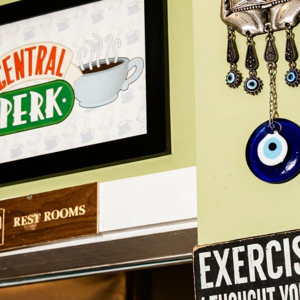 Framed Central Perk coffee sign hangs above a restrooms sign, alongside decorative blue evil eye charms and an exercise-themed plaque.