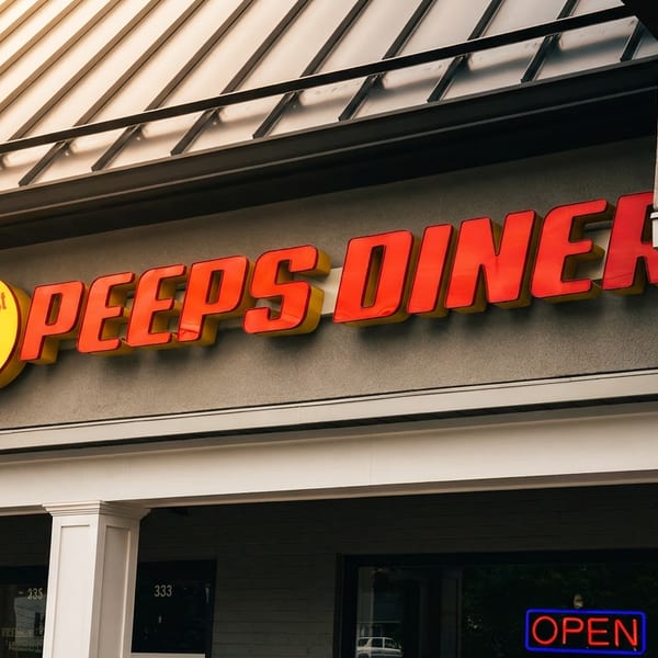 Exterior of Peeps Diner featuring a bold red sign, breakfast and lunch emblem, and illuminated open sign.